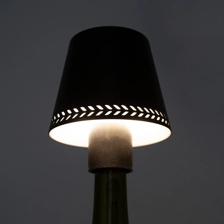 LED-Flaschenaufsatzleuchte in Schwarz auf Weinflasche mit leuchtendem Lochmuster im Schirm
