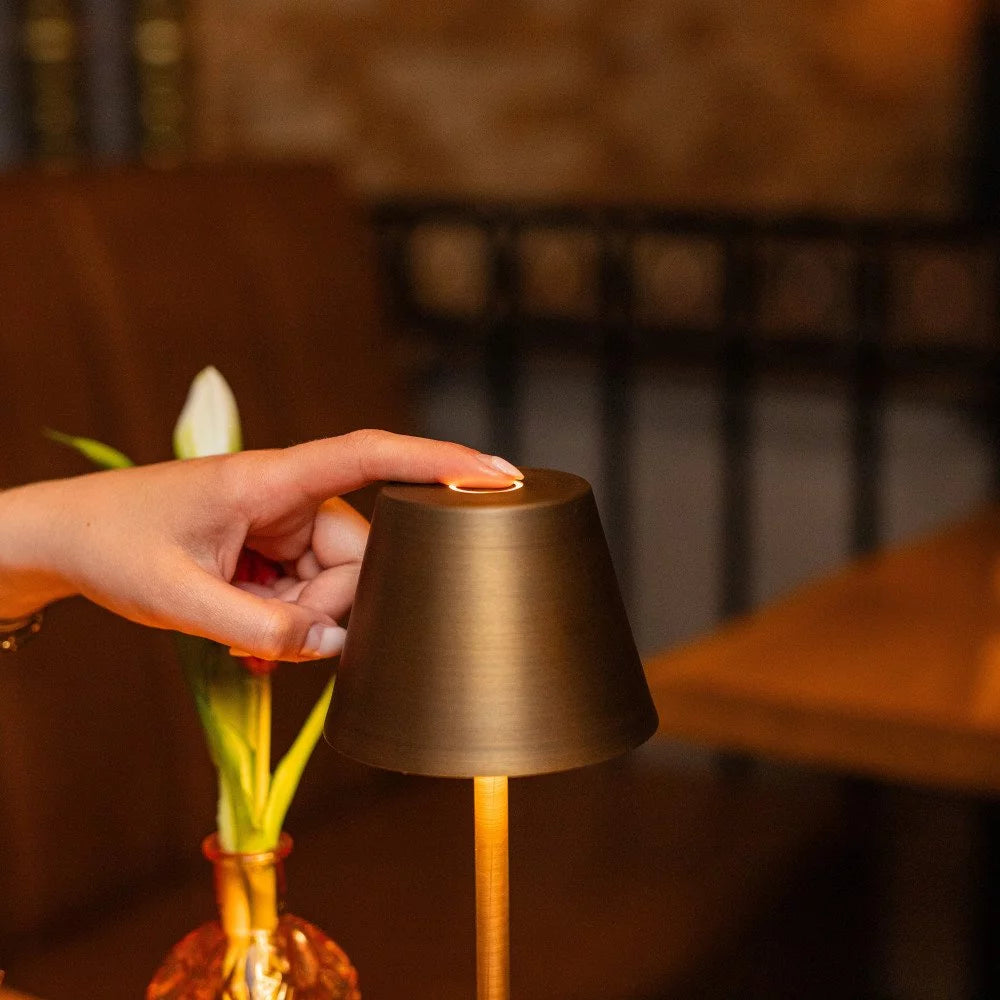 Hand berührt Touch-Sensor der Tischleuchte im warm erleuchteten Bar- und Gastrobereich