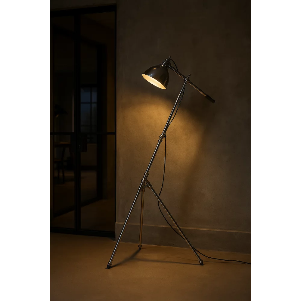 Eingeschaltete Dreibein-Stehlampe in Antiksilber mit warmem Leselicht neben schwarzer Glas-Schiebetür in industriellem Loft