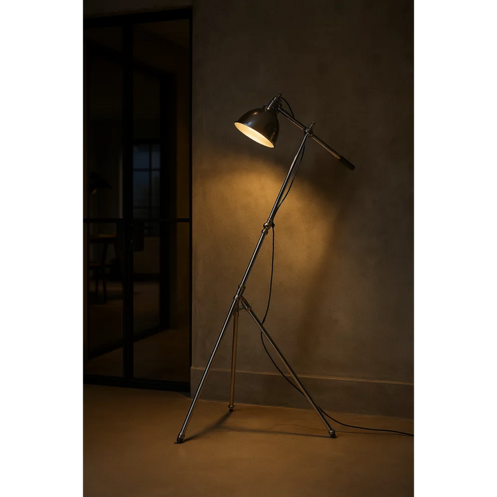 Eingeschaltete Dreibein-Stehlampe in Antiksilber mit warmem Leselicht neben schwarzer Glas-Schiebetür in industriellem Loft