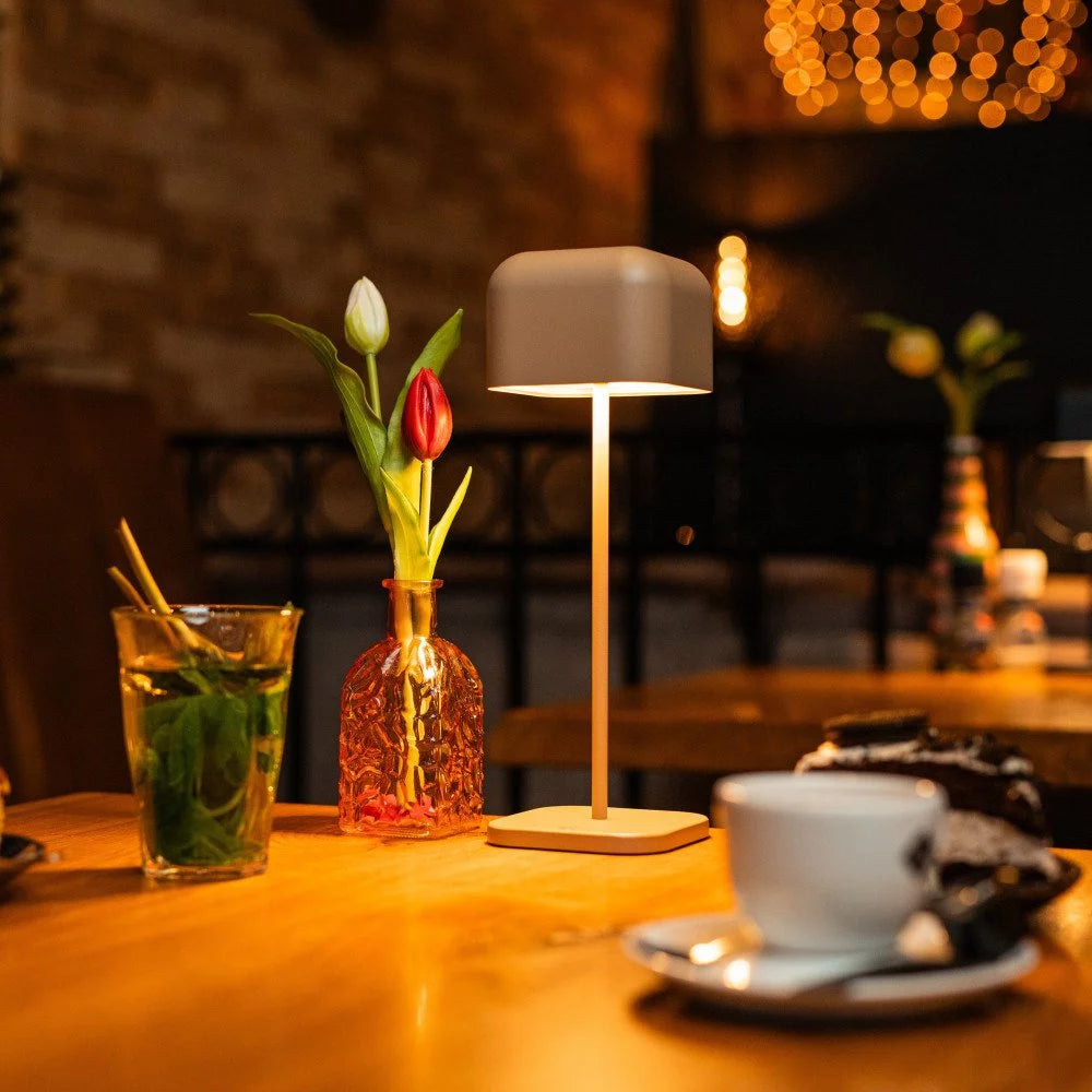 Warmes Ambientelicht der kabellosen Tischlampe auf gedecktem Tisch im gemütlichen Bar-Bereich