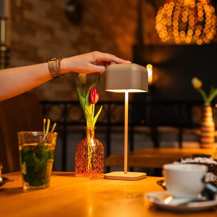 Hand berührt Touch-Sensor der grau-beigen Tischleuchte im stimmungsvoll beleuchteten Restaurant