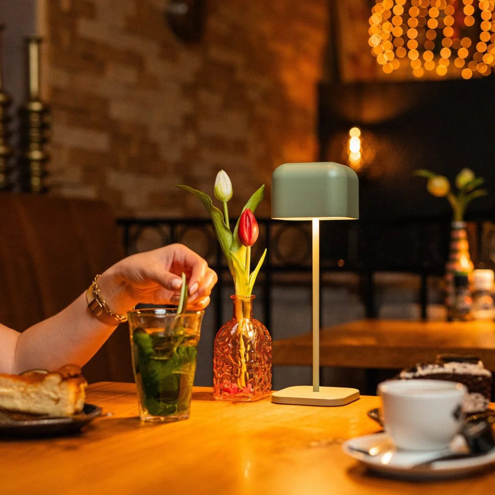 Stimmungsvolles warmes Licht der grüngrauen Tischlampe auf Holztisch mit Blumenvase im Café