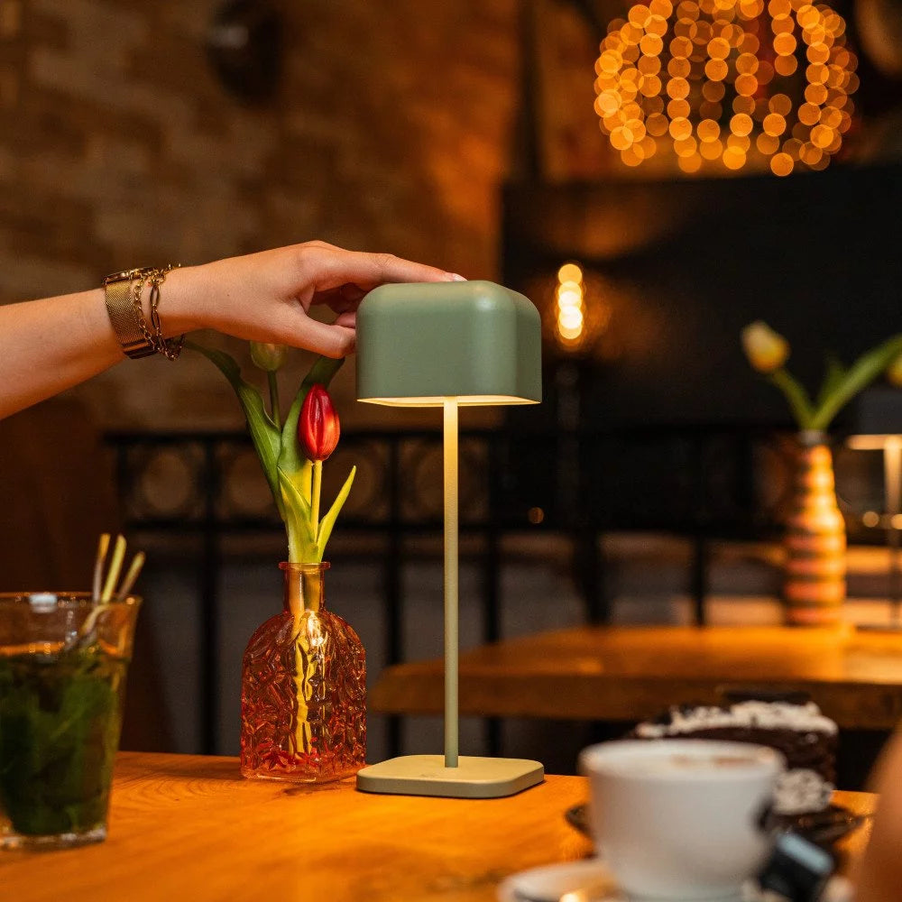 Bedienung der grüngrauen Tischleuchte durch Berühren des oberen Touch-Sensors im Restaurant