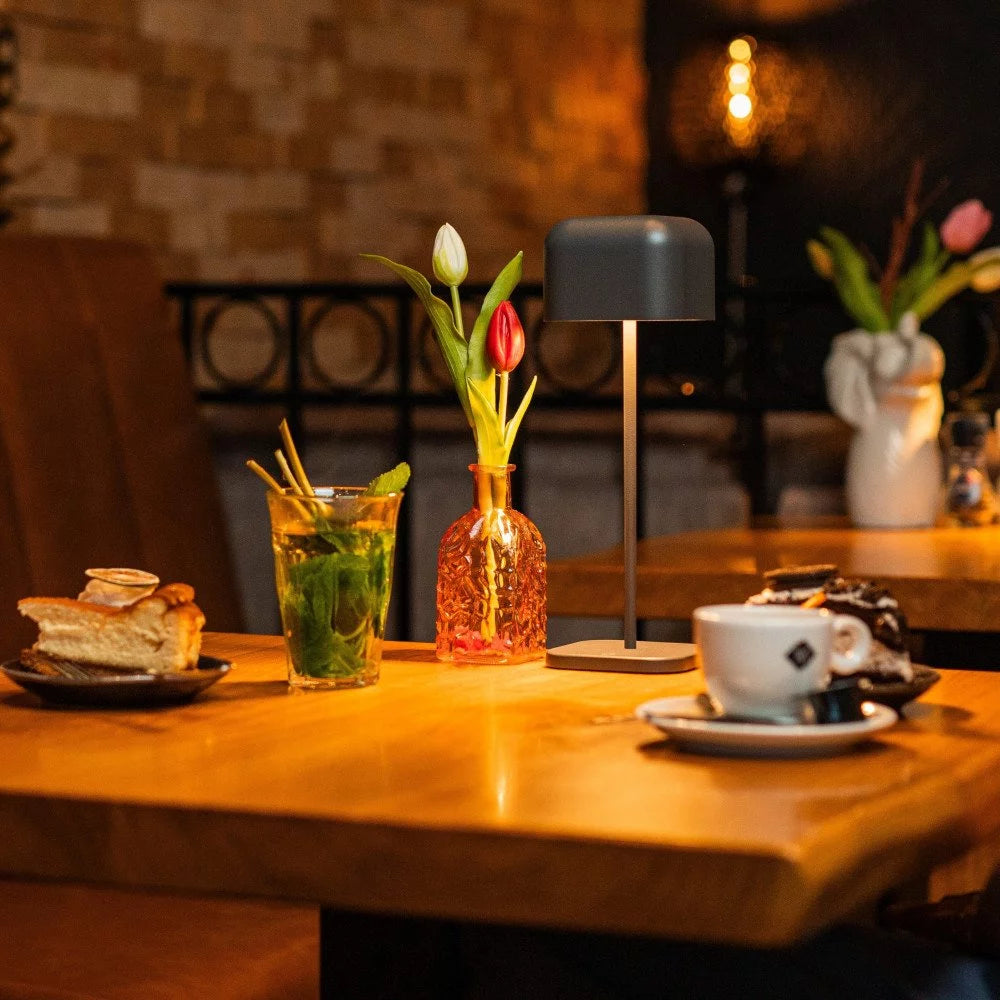 Stimmungsvolles Café-Ambiente mit der anthrazitfarbenen Akkuleuchte, Kaffeetasse und Kuchen