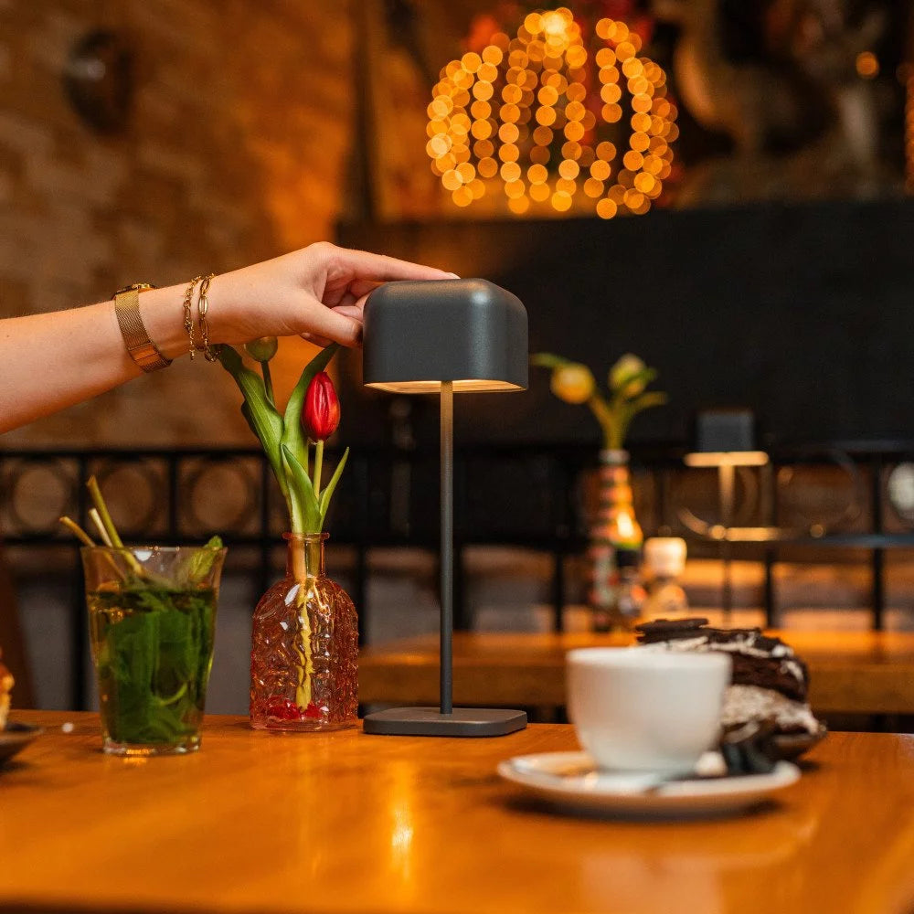 Frauenhand drückt Einschaltknopf kabellose Tischlampe Cabo Medium Anthrazit im Restaurant