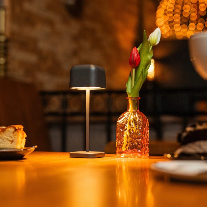 Gemütliche Tischszene im Restaurant mit anthrazitfarbener Akkuleuchte, Minztee und Kuchen
