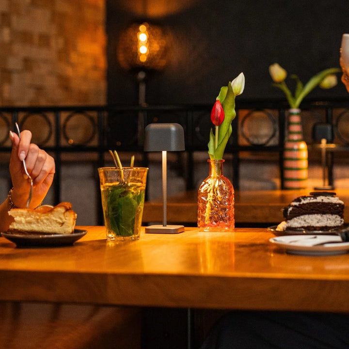 Stimmungsvolles warmes Licht der anthrazitfarbenen Tischleuchte auf Holztisch im Café-Ambiente