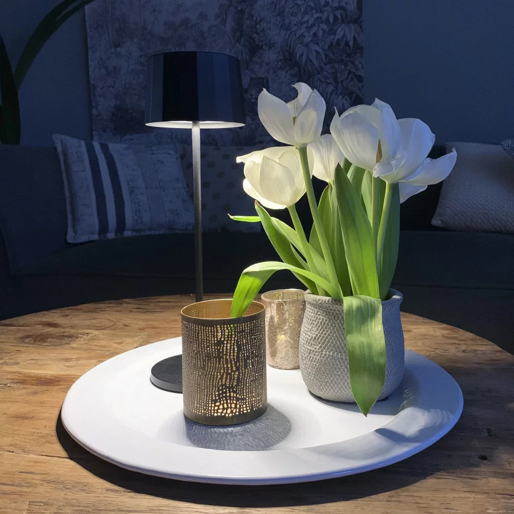 Kabellose Tischlampe Lido Corten leuchtend auf weißem Teller mit Blumen – romantisches Stimmungslicht