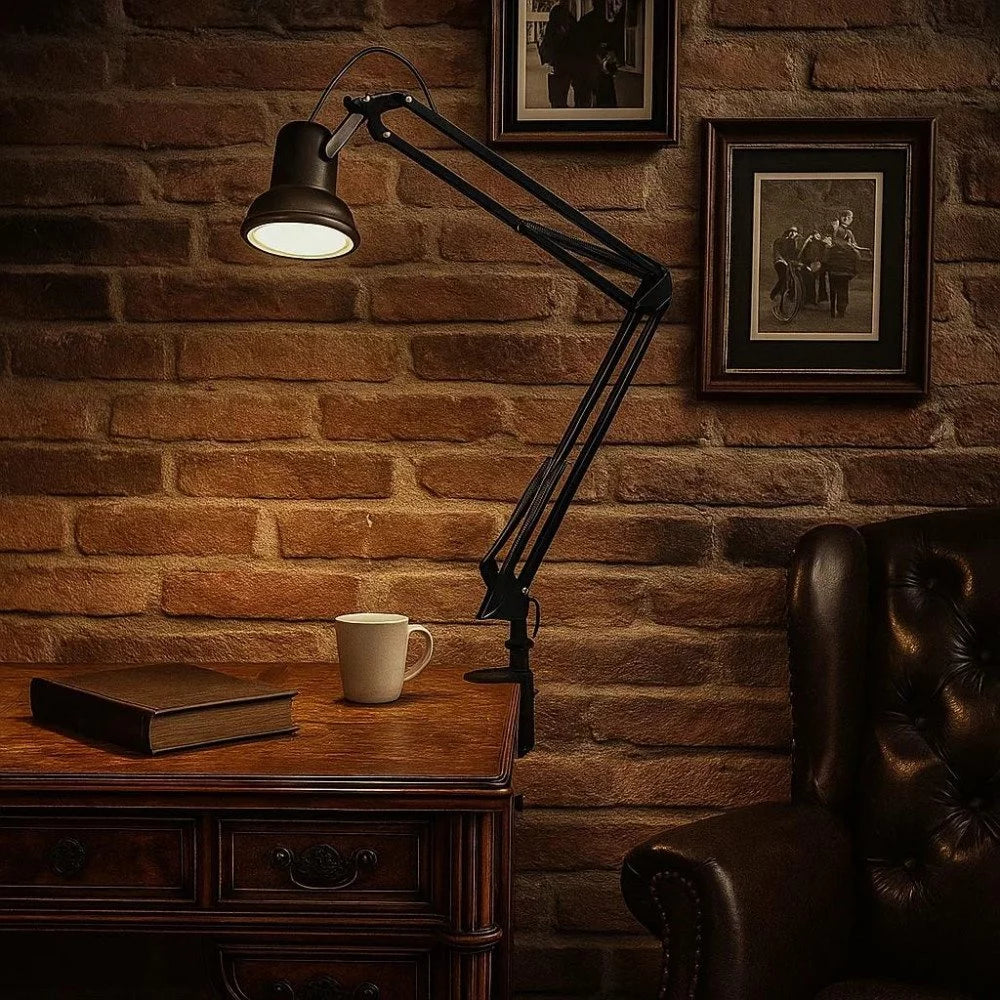 Vintage Federzug-Klemmlampe in Antikschwarz leuchtet über Schreibtisch mit Kaffeetasse und Buch vor Ziegelwand