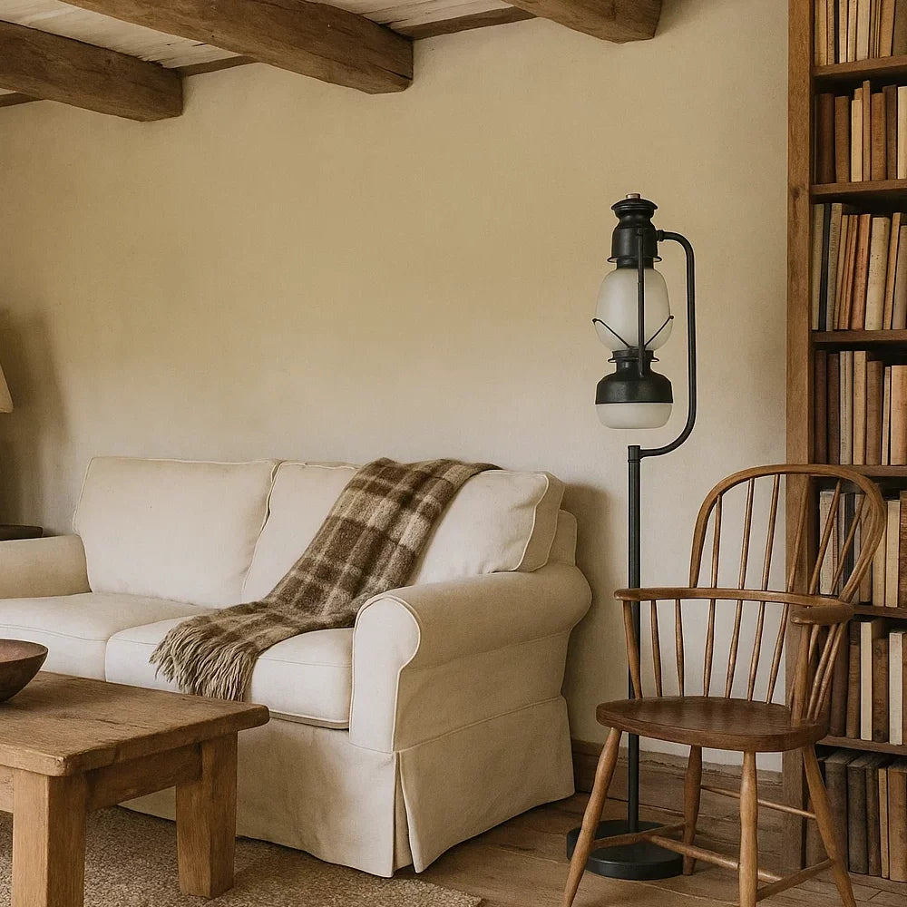 Schwarze Vintage-Laternen-Stehlampe mit Opalglaszylinder neben hellem Stoffsofa, Holzstuhl und Bücherregal im Landhaus-Wohnzimmer