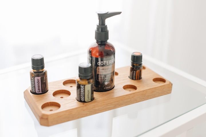 Eichenholz-Organizer auf weißem Glastisch mit zentraler Pumpspenderflasche und Tropffläschchen für Aromatherapie