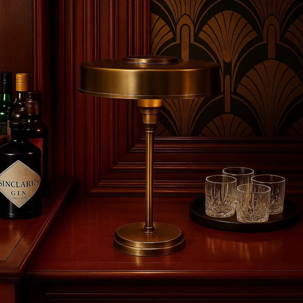 Messing-Tischlampe neben Gin-Flasche und Kristallgläsern auf Holzkommode mit 20er-Jahre-Tapete