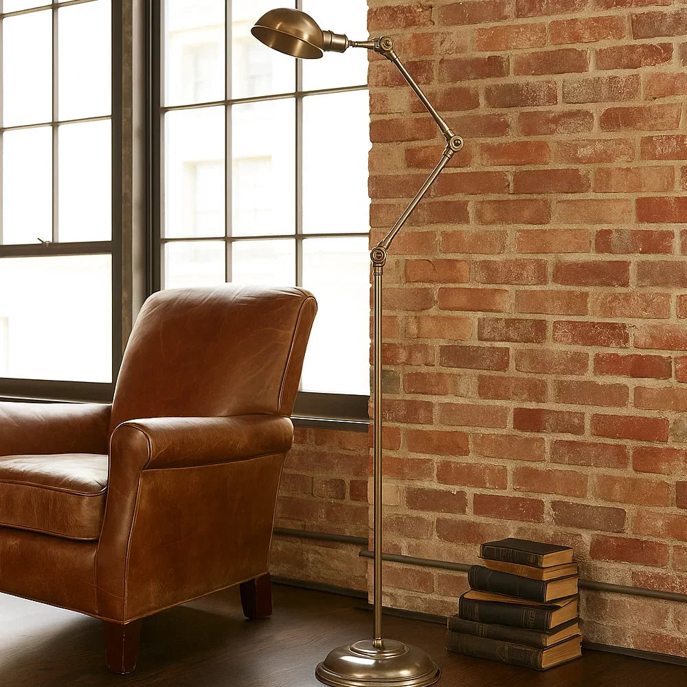 Klassische Gelenk-Stehlampe in Antikmessing neben braunem Ledersessel vor Backsteinwand im Loft