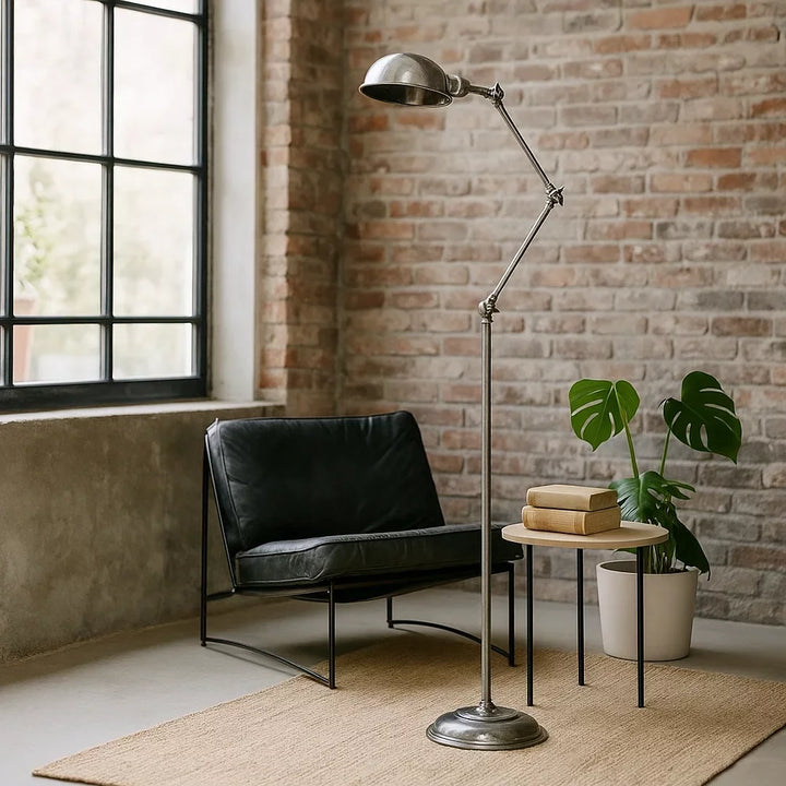 Industrielle Gelenk-Stehlampe in Antiksilber neben schwarzem Ledersessel vor Backsteinwand im Loft