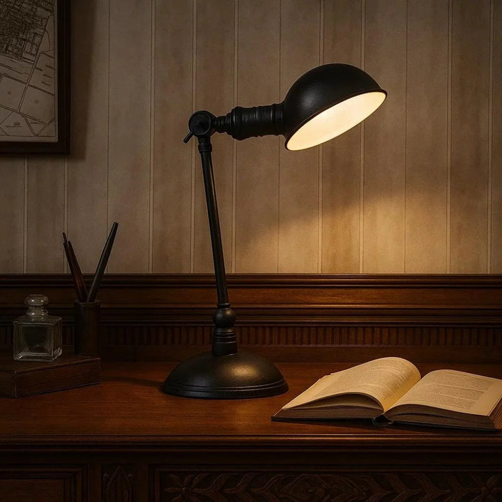 Klassische Schreibtischleuchte in Antikschwarz eingeschaltet über aufgeschlagenem Buch auf dunklem Holztisch