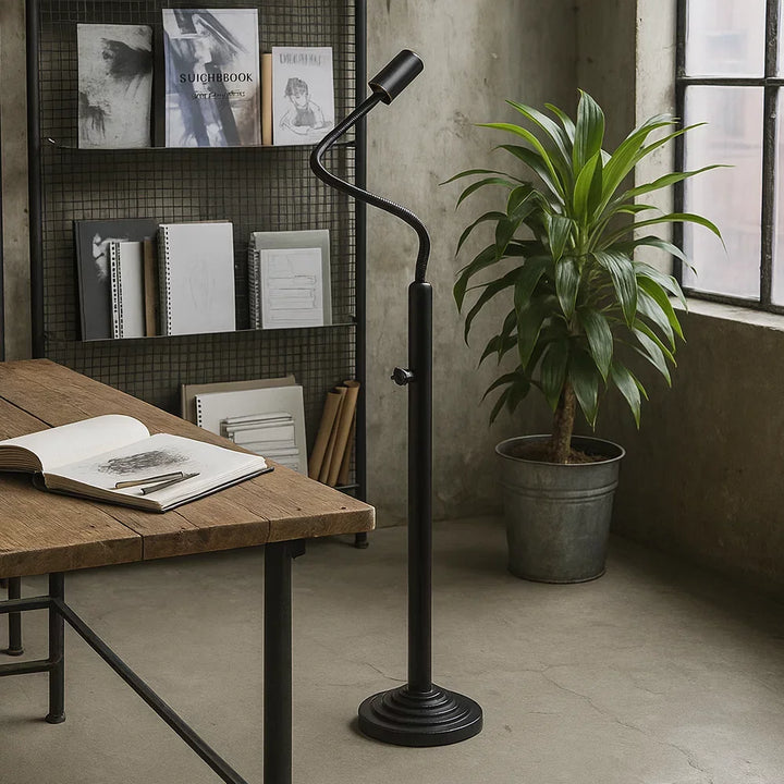 Industrielle Flexarm-Stehlampe in Mattschwarz neben Zeichentisch aus Holz, Skizzenbuch, Gitterregal und Zimmerpflanze im Künstler-Atelier