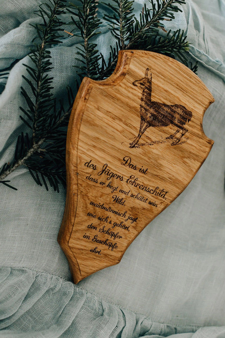 Geöltes Eichenholz-Trophäenschild mit Gams-Gravur neben einem echten Tannenzweig